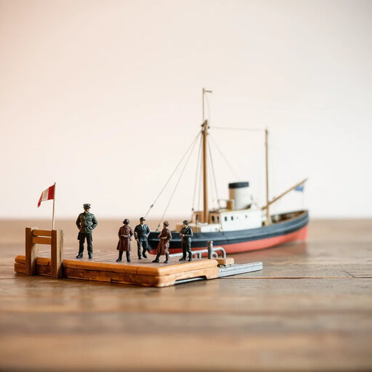 Scale model figures standing by a miniature pier beside a docked ship model